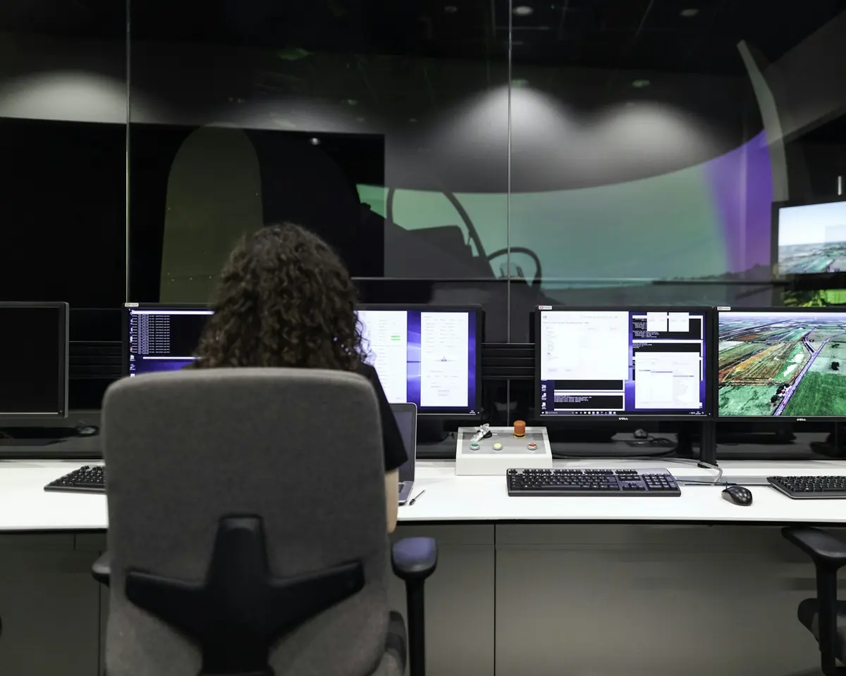 Engenheira de costas monitora várias telas com dados em uma sala de controle