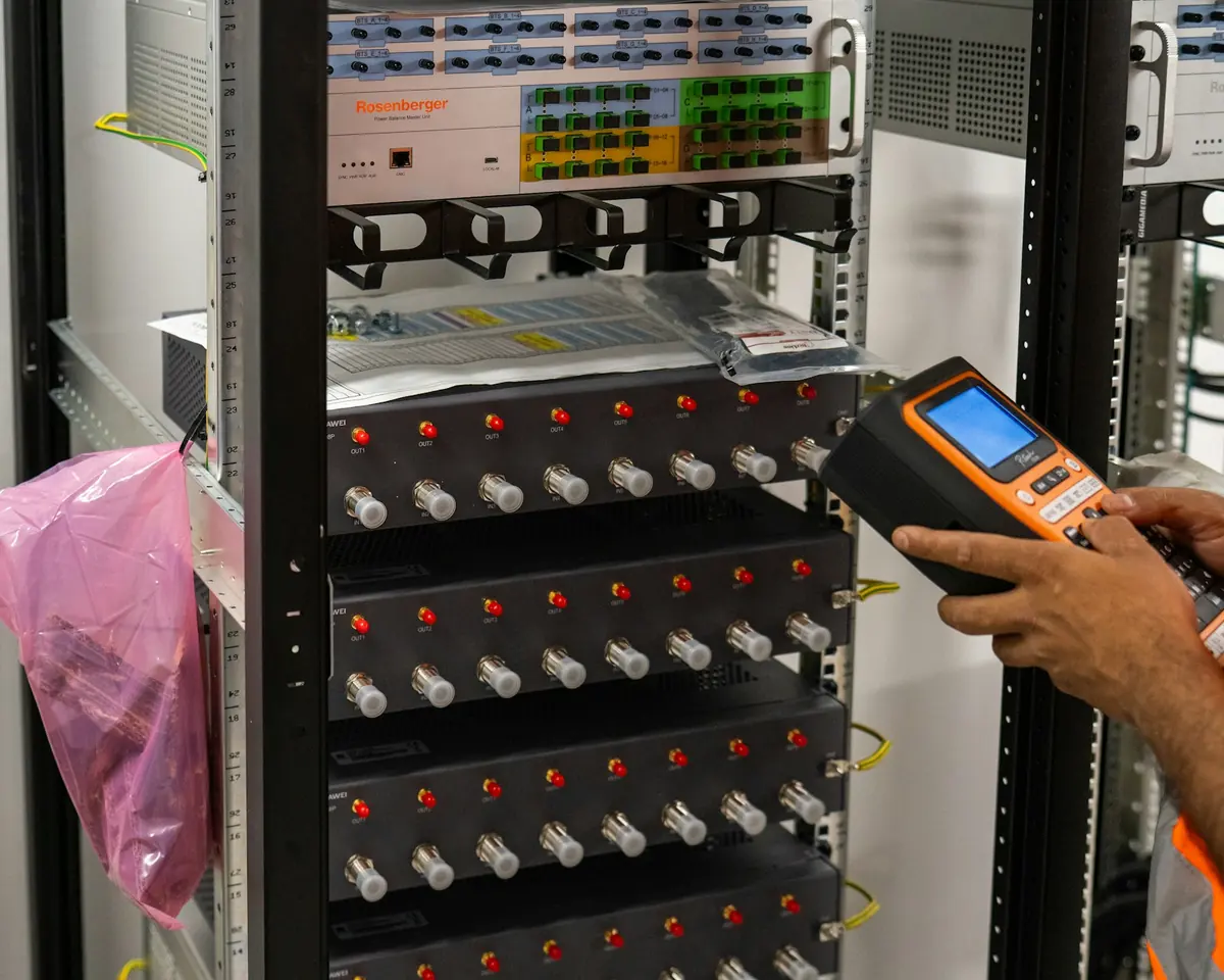 Técnico com aparelho de medição trabalha em um rack de distribuição de fibra óptica