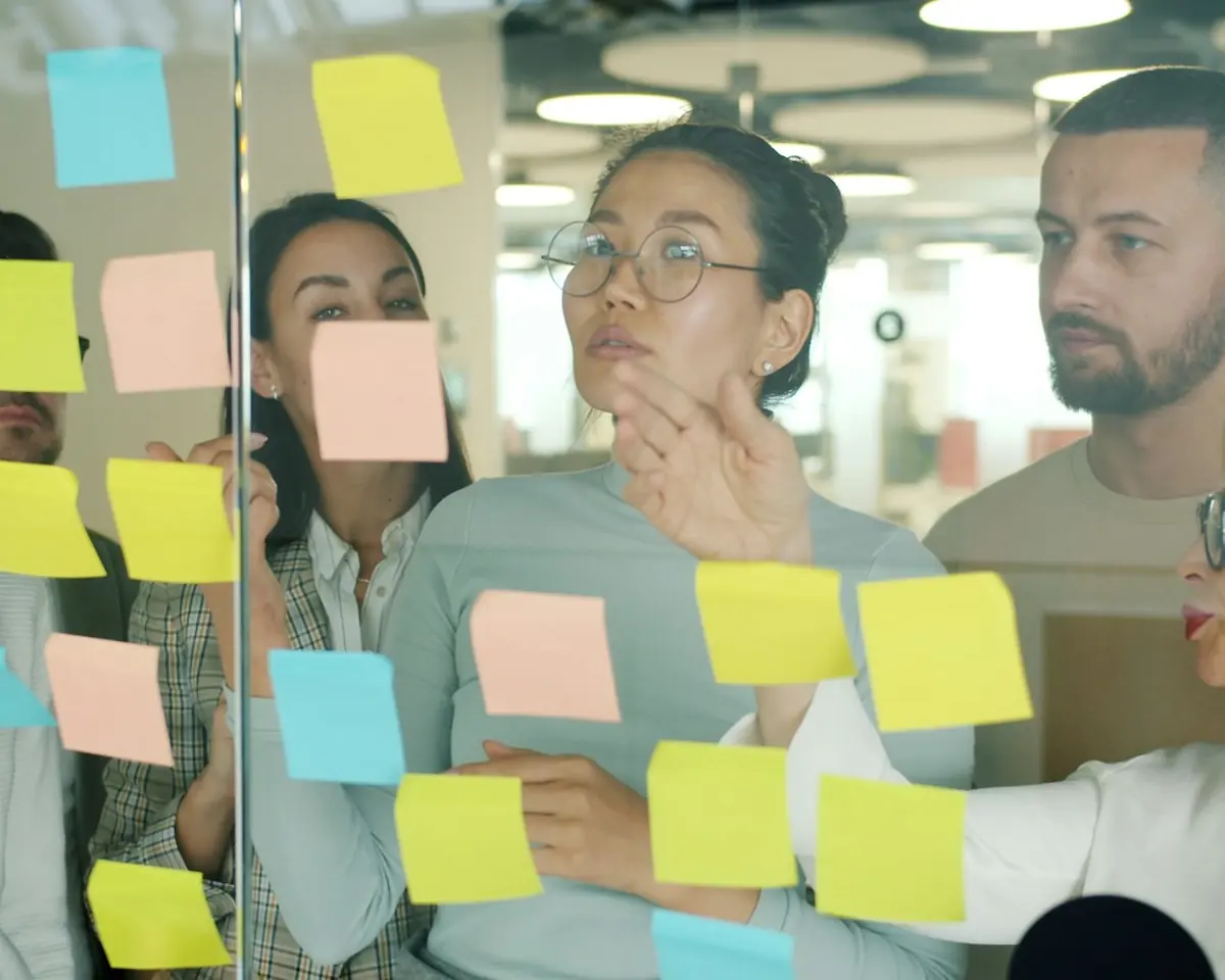 Equipe organiza ideias em notas adesivas num painel de vidro, concentrada no planejamento